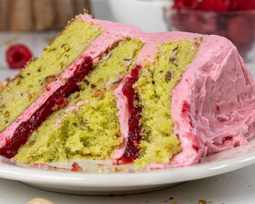 image of a raspberry pistachio cake slice that's been cut into to show it's filling and tender cake layers