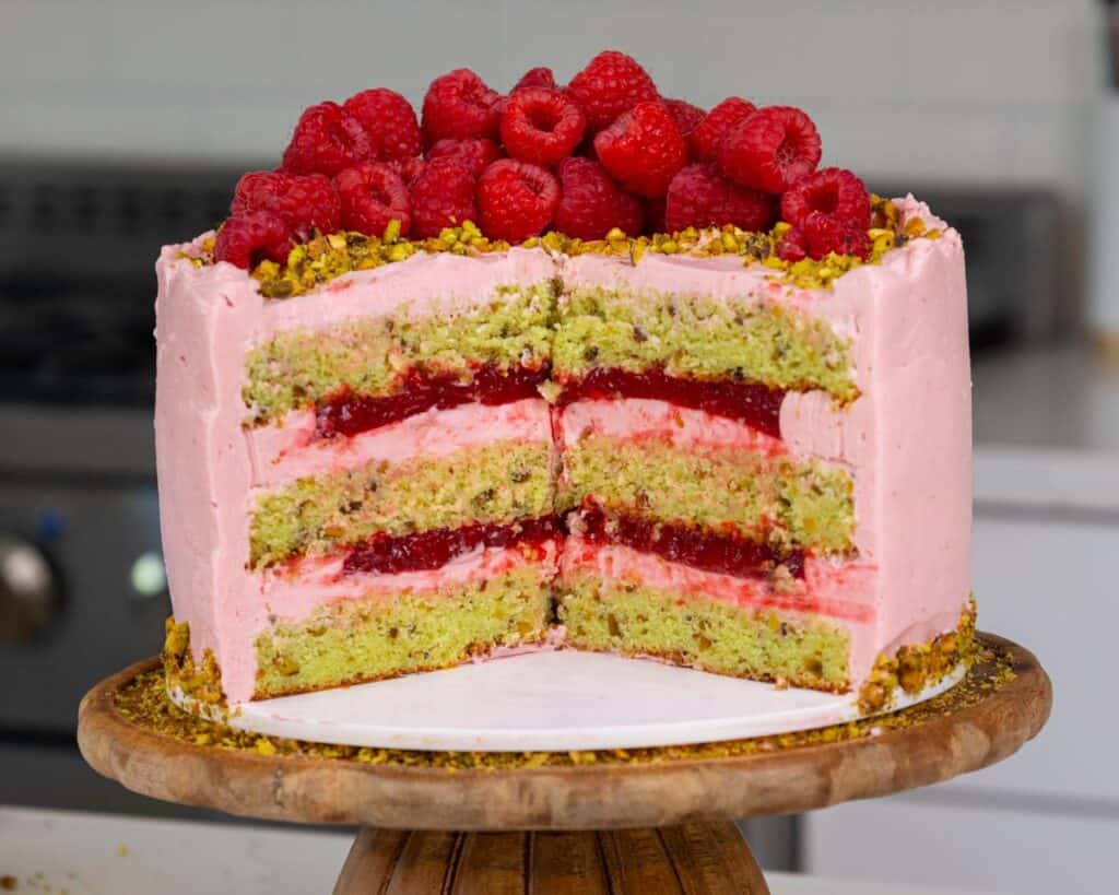 image of a raspberry pistachio cake that's been cut into to show it's filling and tender cake layers