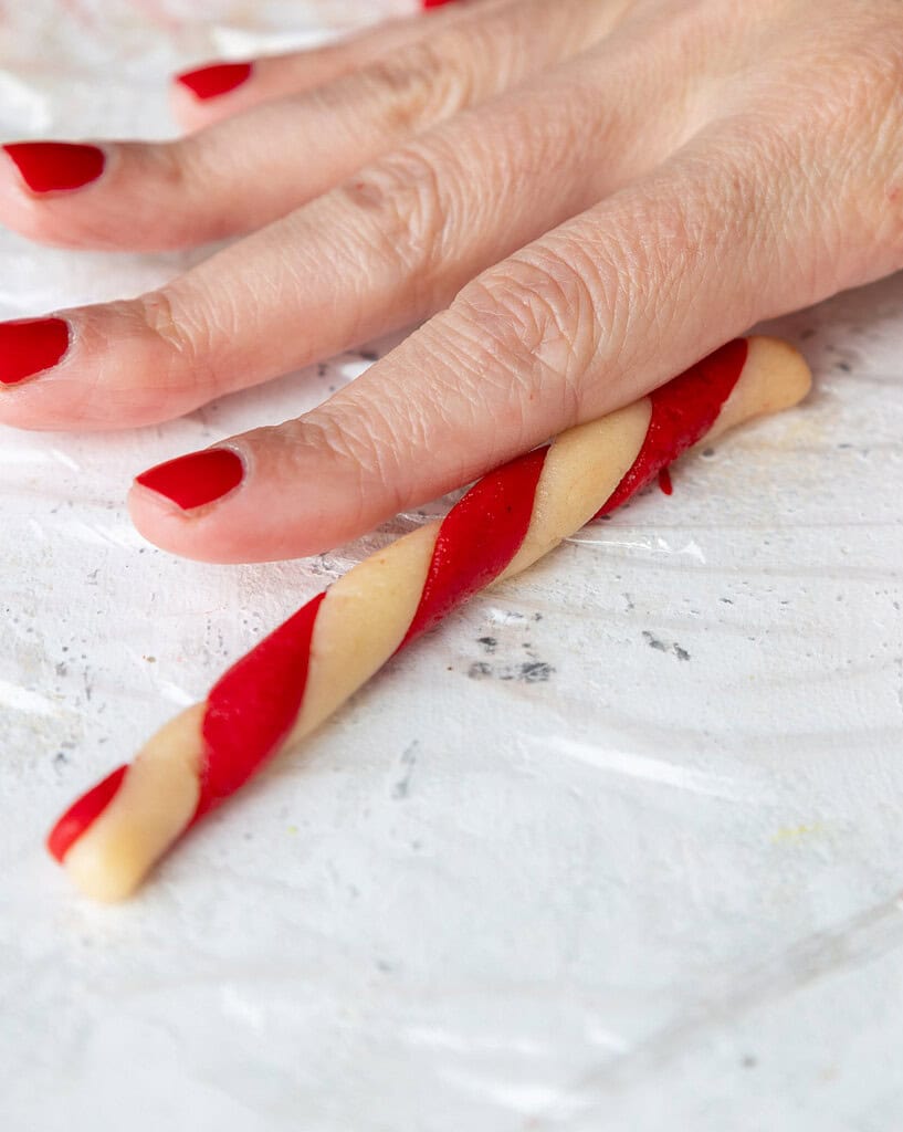 image of red and white cookie dough being rolled together to make a candy cane cookie