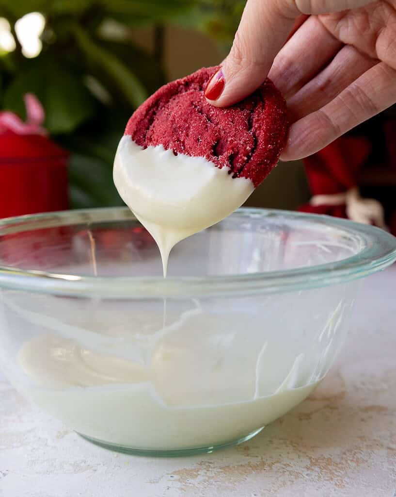 image of a red velvet sugar cookie being dipped in white chocolate