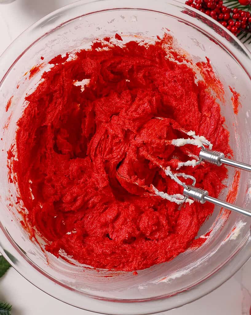 image of an egg and red gel food coloring being mixed into creamed sugar and butter
