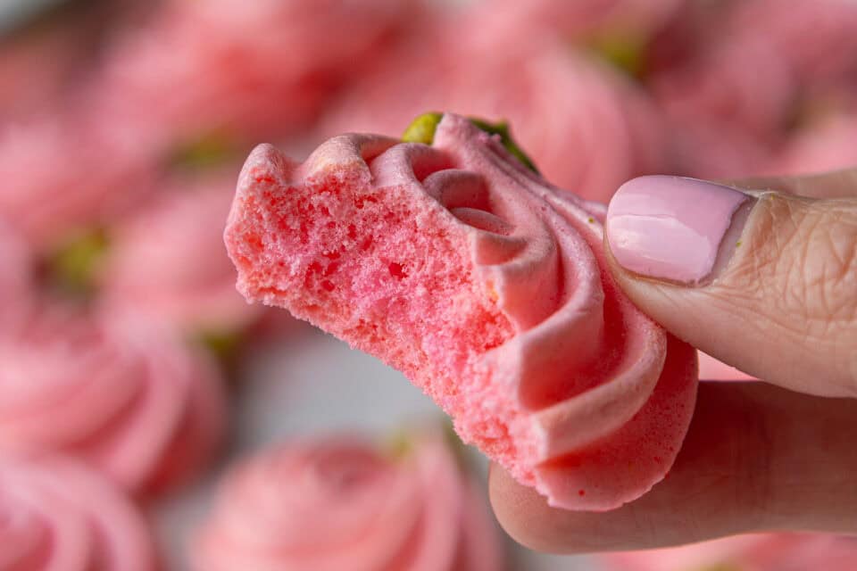 image of a pink meringue rose that's been bitten into to show it's crisp, airy center