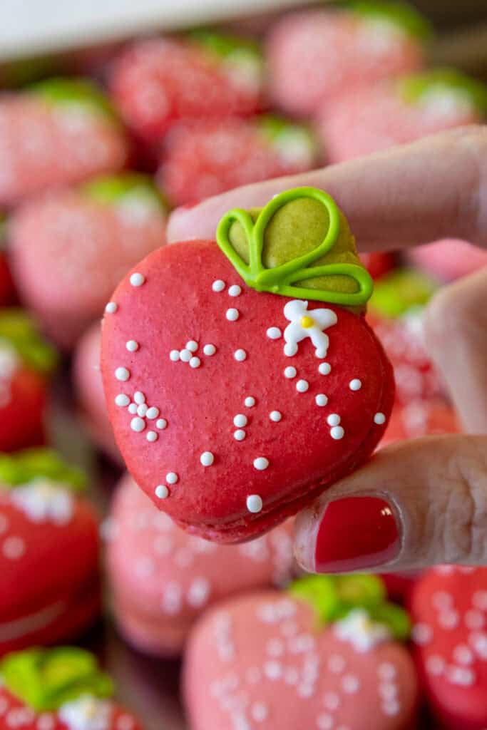 image of a strawberry macaron that's been decorated with white sprinkles and royal icing