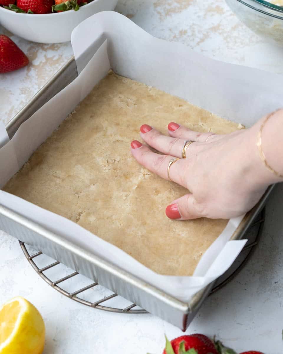 image of shortbread crust being pressed into an 8x8-inch metal baking dish