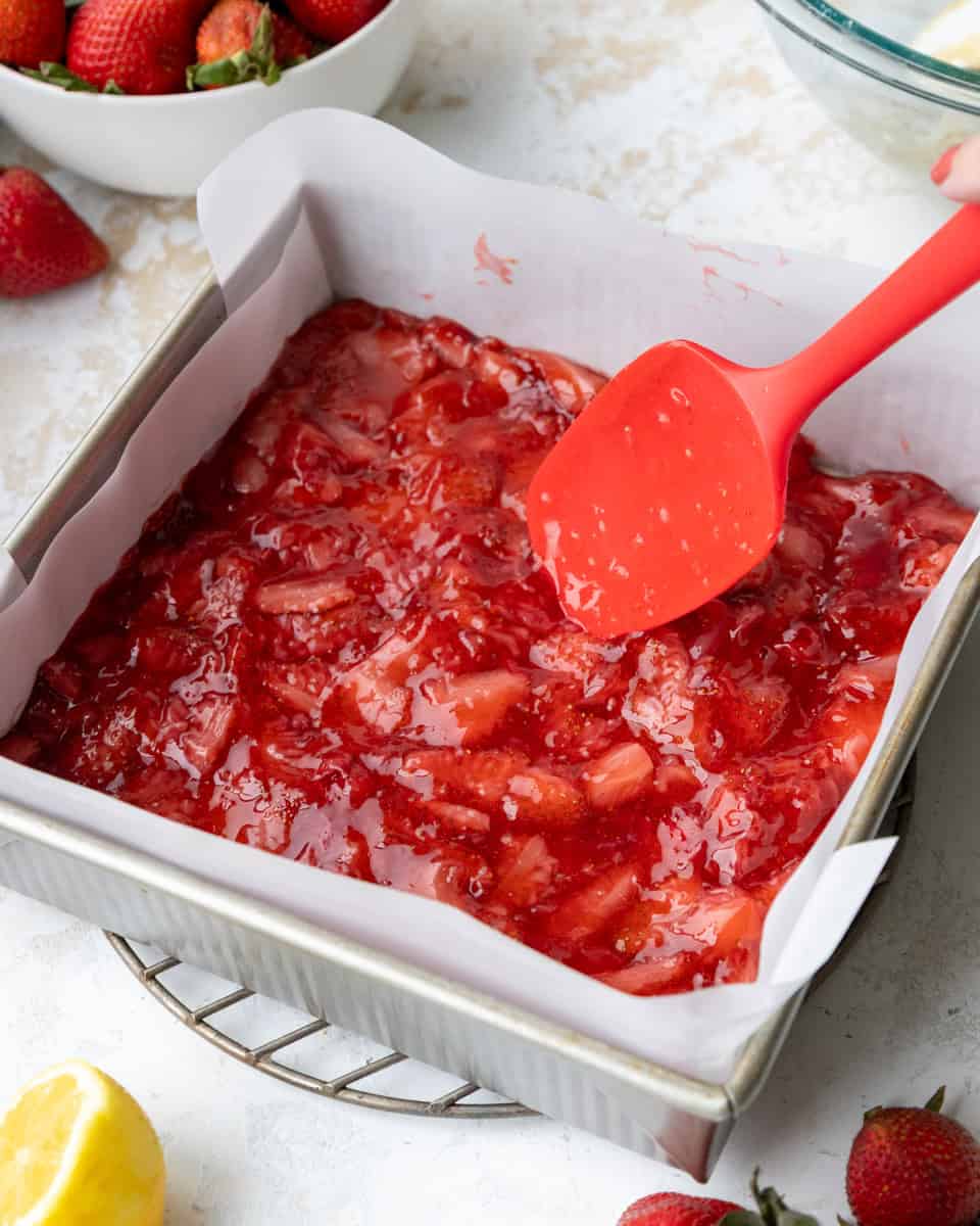image of strawberry filling being added on top of a shortbread crust to make strawberry crumble bars