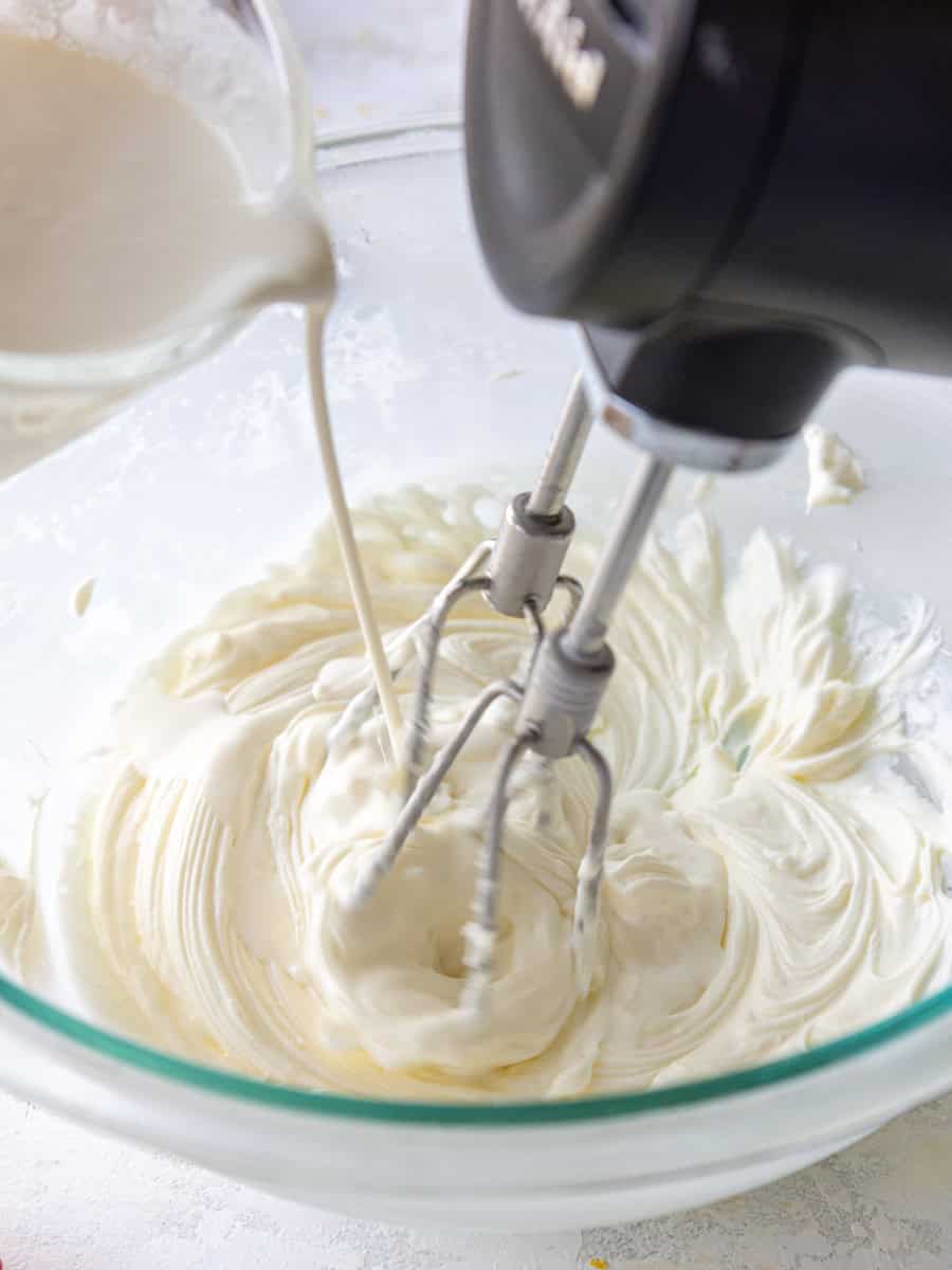 image of heavy cream being poured into beaten cream cheese to make whipped cream frosting
