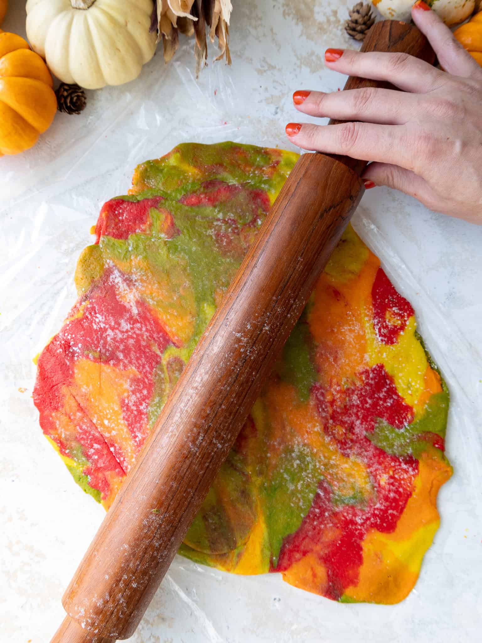 image of multicolored marbled cookie dough being rolled out with a rolling pin