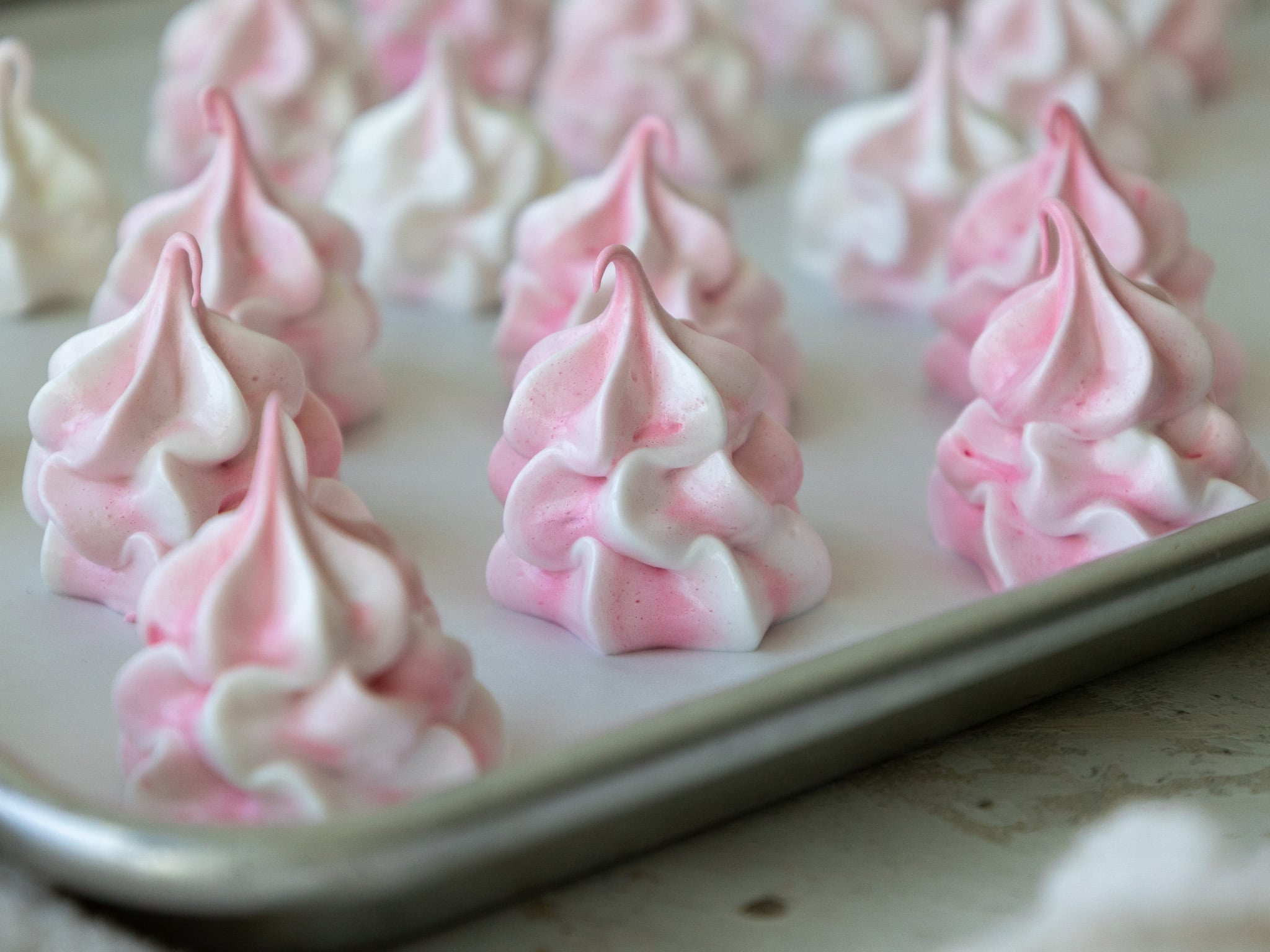 image of pink meringue cookies piped onto a parchment-lined baking sheet